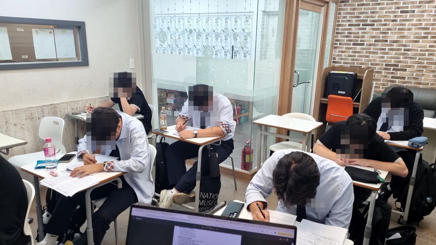 교복 차림 학생들이 유리벽 강의실에서 문제를 풀고 있는 장면